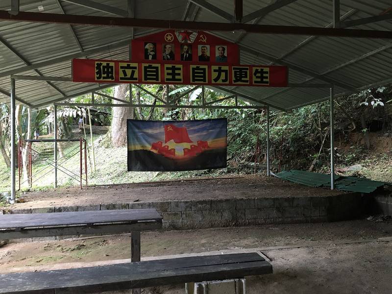 โรงเรือนหลังคาสังกะสีโล่ง ๆ มีป้ายผ้าสีแดงอักษรจีนแขวนด้านหน้า